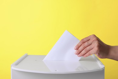 Woman putting her vote into ballot box against yellow background, closeup