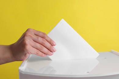 Woman putting her vote into ballot box against yellow background, closeup