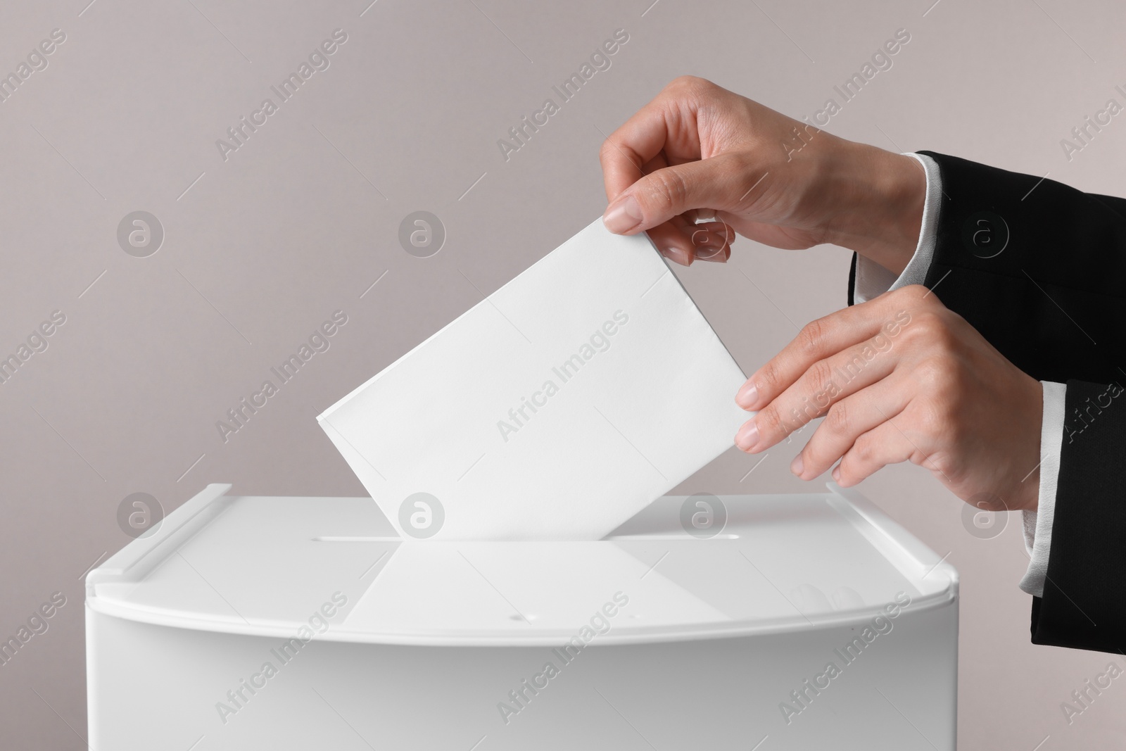 Photo of Woman putting her vote into ballot box against grey background, closeup