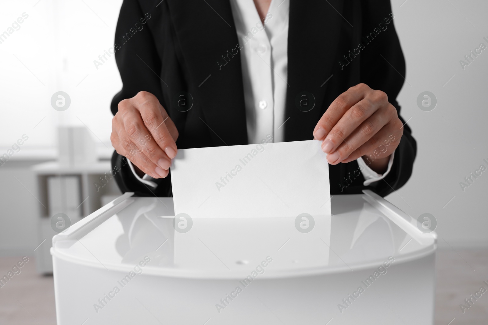 Photo of Woman putting her vote into ballot box indoors, closeup