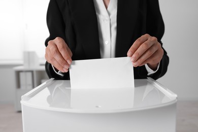 Woman putting her vote into ballot box indoors, closeup