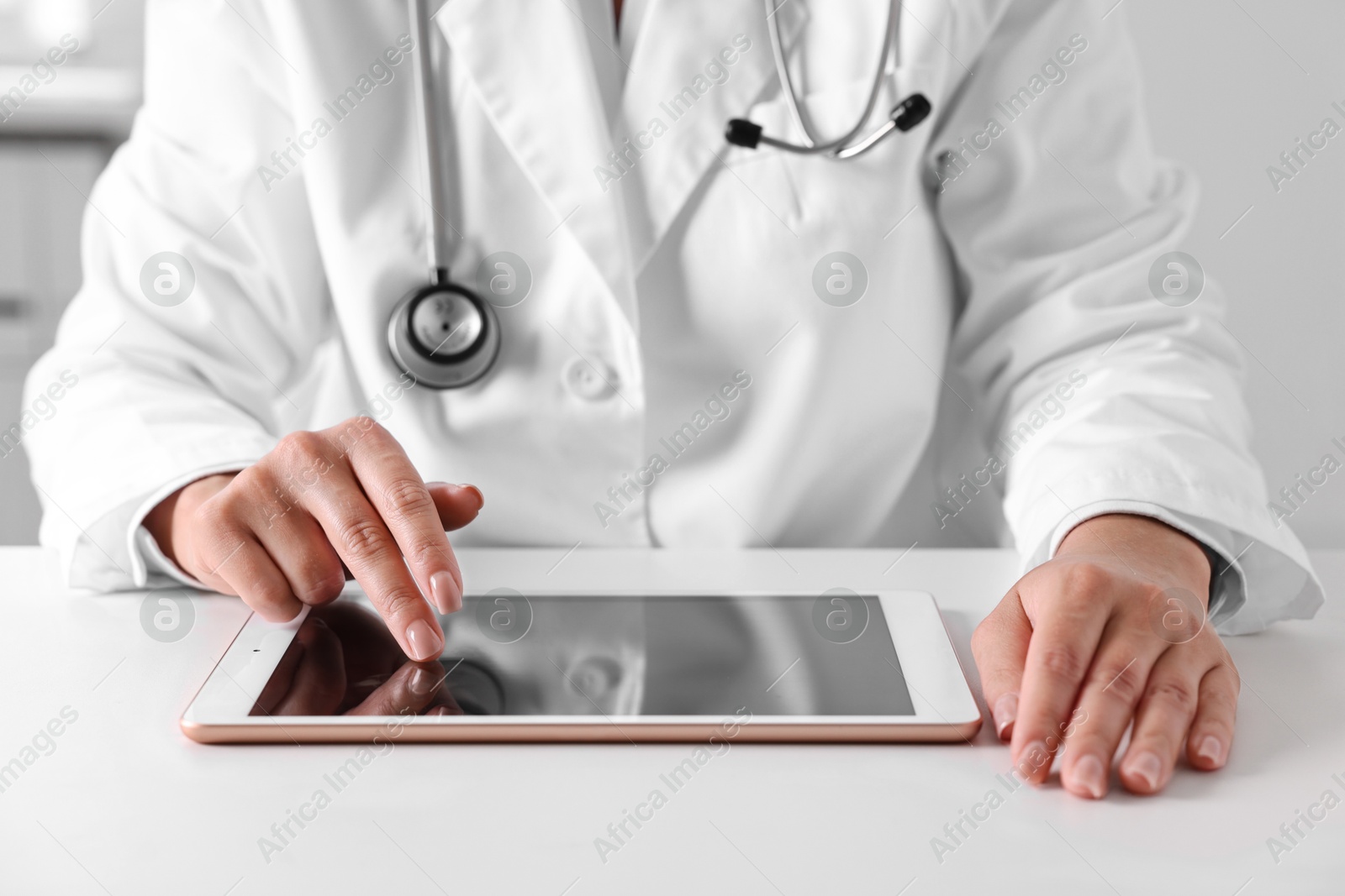 Photo of Doctor with tablet at table in clinic, closeup view