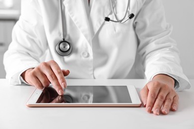 Photo of Doctor with tablet at table in clinic, closeup view