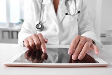 Photo of Doctor with tablet at table in clinic, closeup view