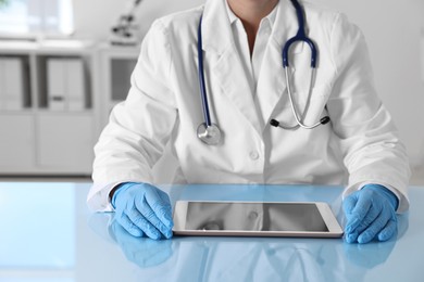 Doctor with tablet at table in clinic, closeup view