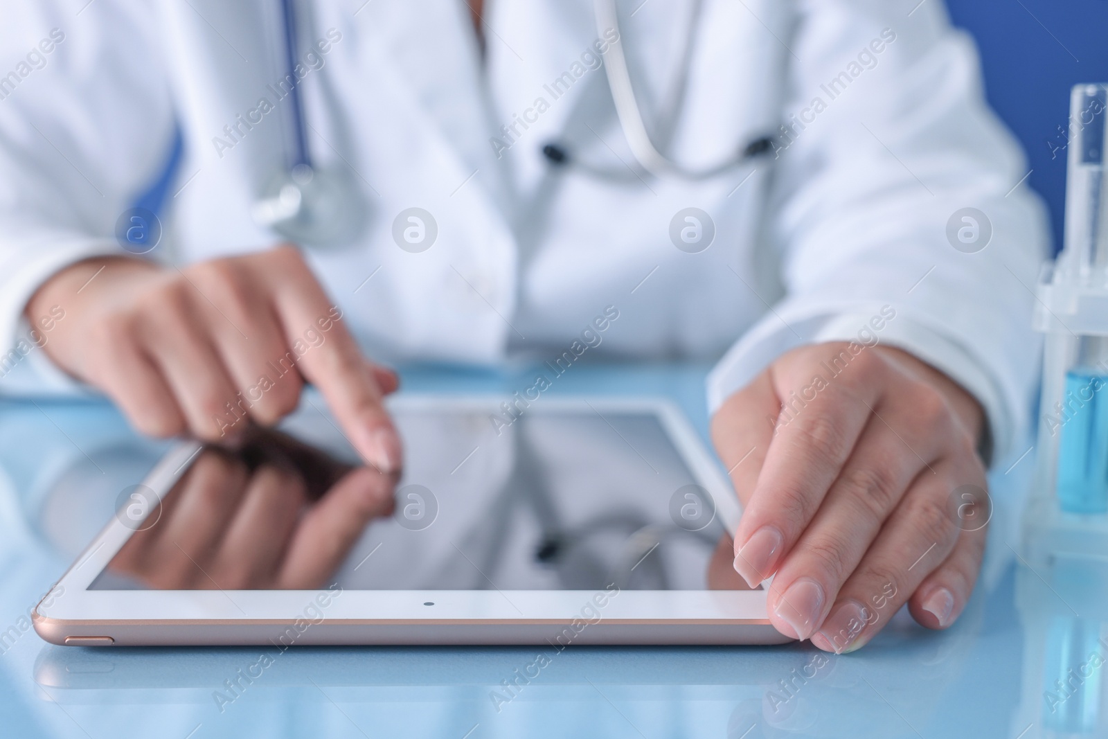 Photo of Doctor with tablet at table against blue background, closeup view