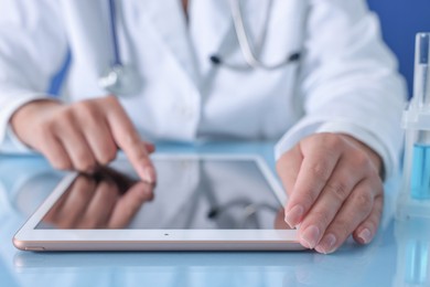 Doctor with tablet at table against blue background, closeup view