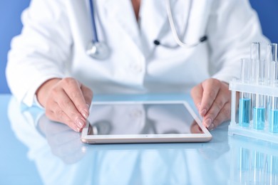 Photo of Doctor with tablet at table against blue background, closeup view