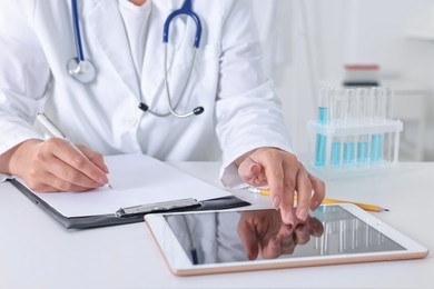 Doctor with tablet at table in clinic, closeup view