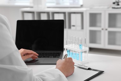 Doctor with laptop at table in clinic, closeup view