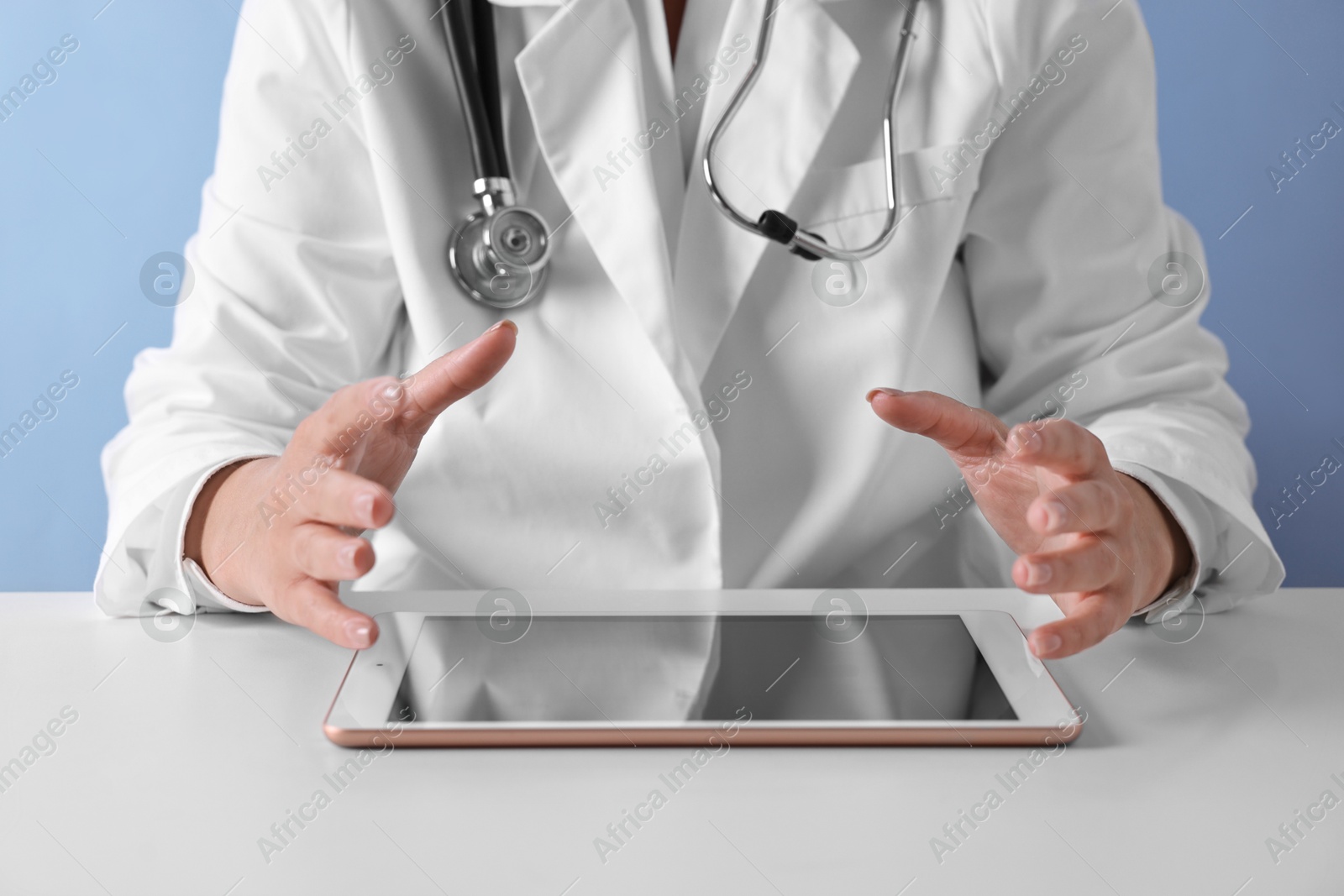 Photo of Doctor with tablet at table against light blue background, closeup view