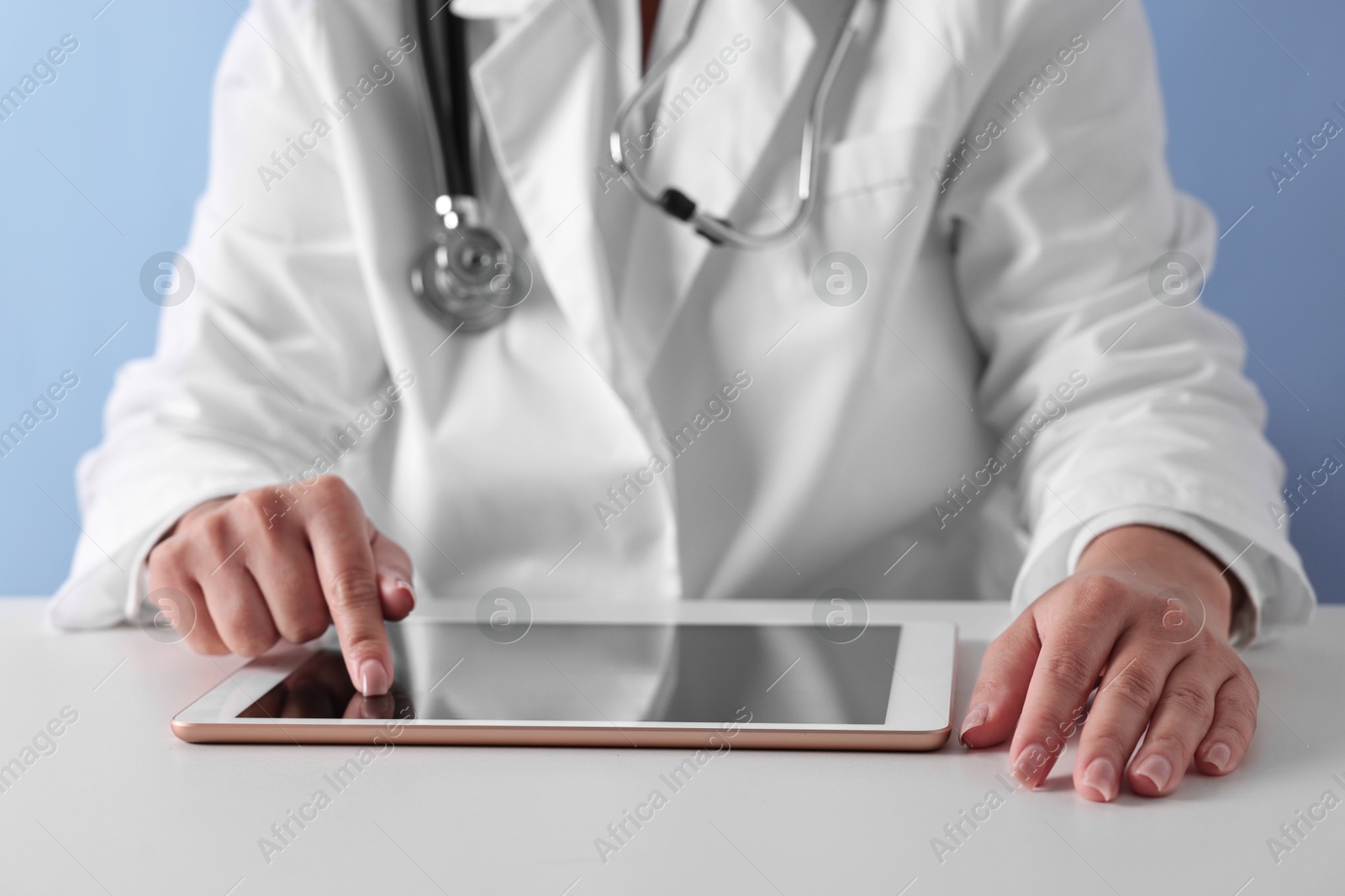 Photo of Doctor with tablet at table against light blue background, closeup view