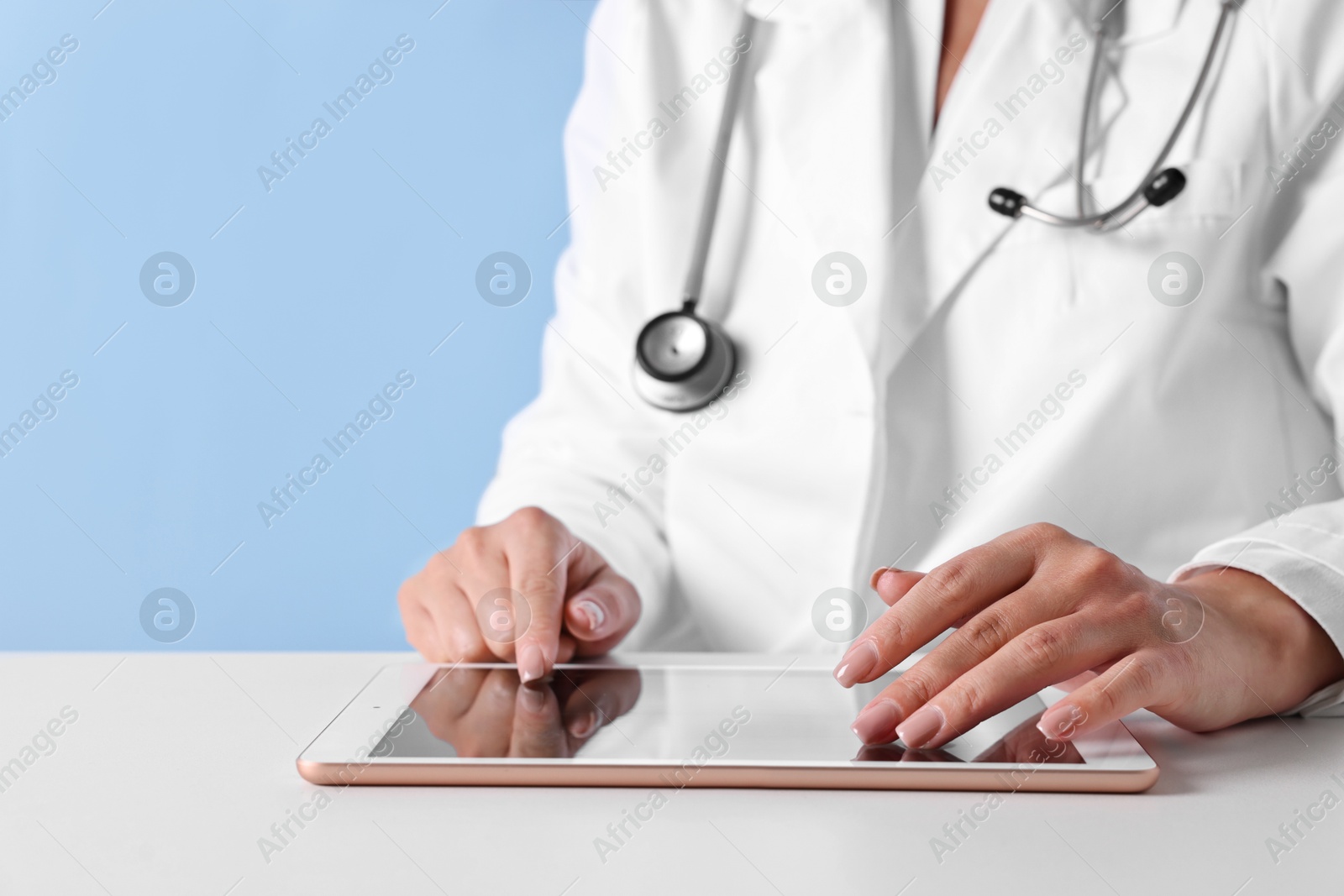 Photo of Doctor with tablet at table against light blue background, closeup view