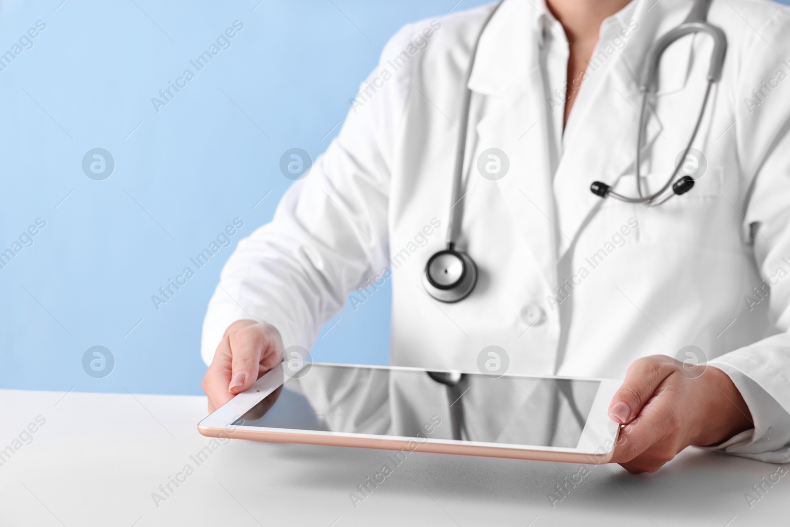 Photo of Doctor with tablet at table against light blue background, closeup view