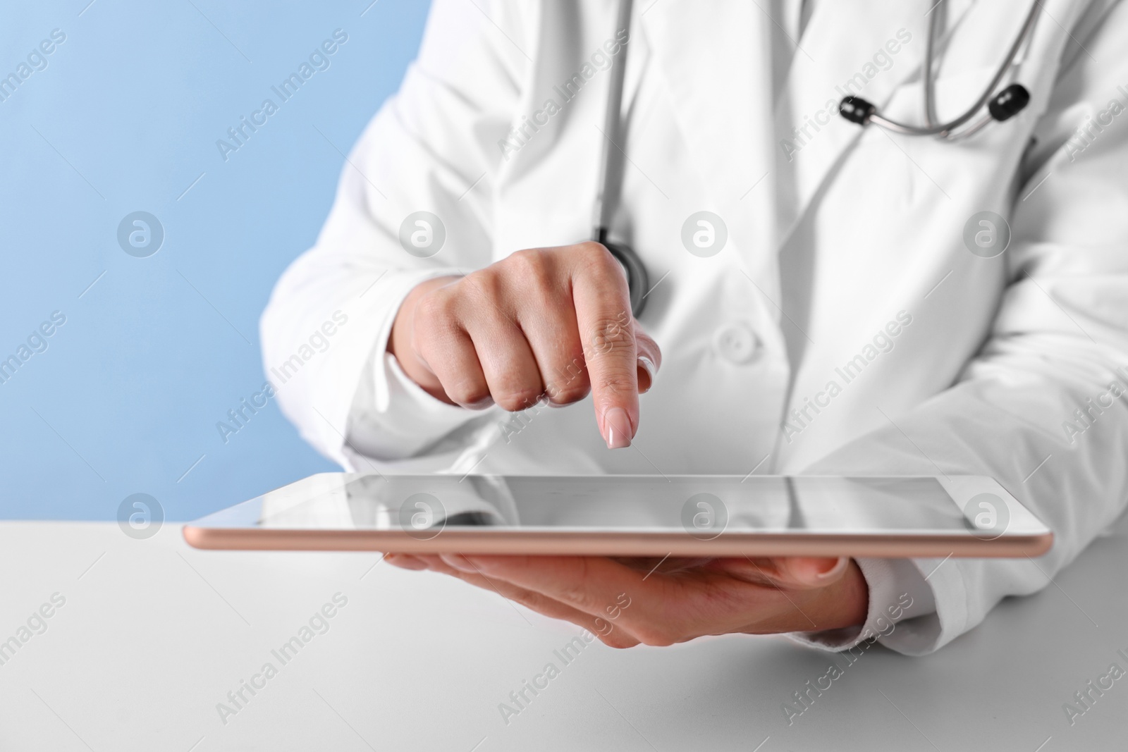 Photo of Doctor with tablet at table against light blue background, closeup view