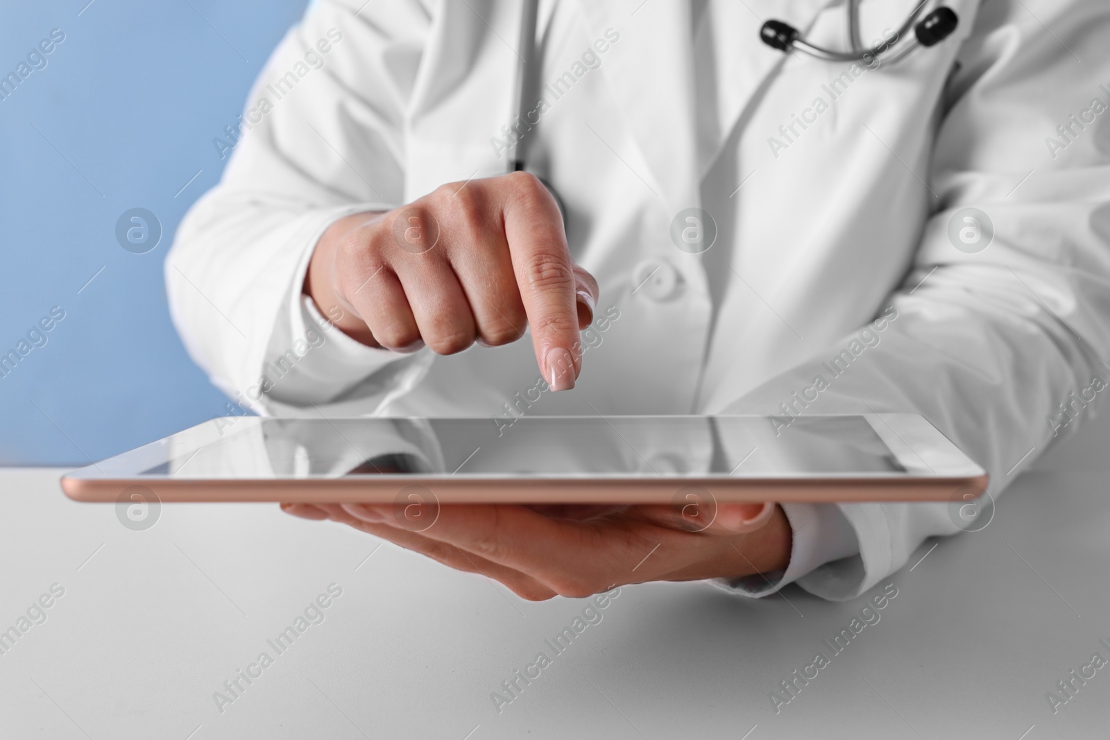 Photo of Doctor with tablet at table against light blue background, closeup view