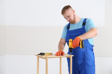 Photo of Worker with electric screwdriver assembling furniture indoors. Space for text