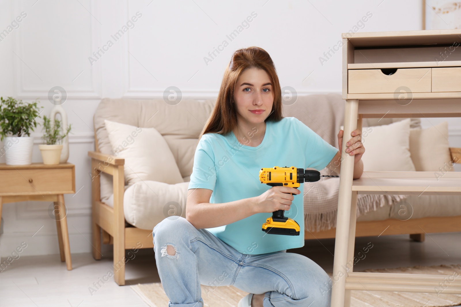 Photo of Woman with electric screwdriver assembling table in room