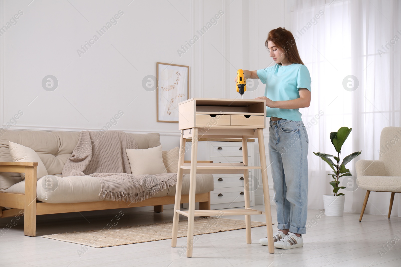 Photo of Woman with electric screwdriver assembling table in room