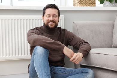 Happy man near heating radiator at home