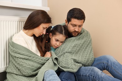 Family with blanket warming up near heating radiator at home