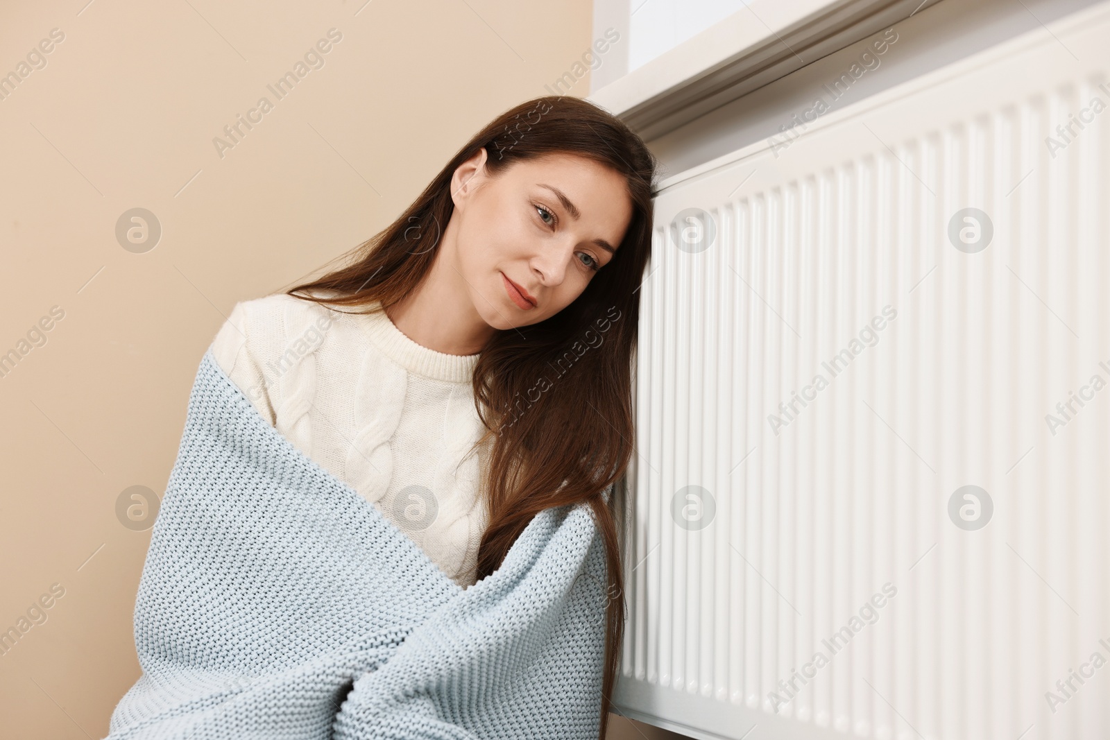 Photo of Woman with blanket warming near heating radiator at home