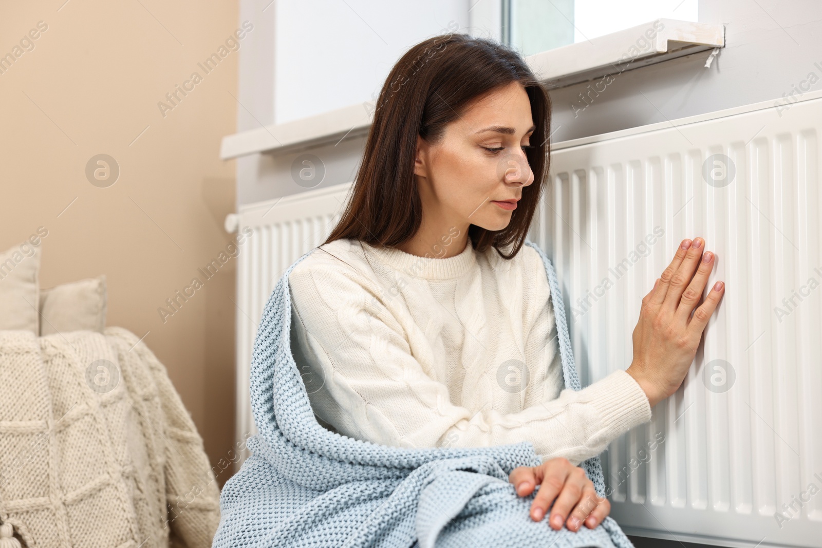 Photo of Woman with blanket warming near heating radiator at home