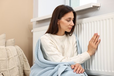 Woman with blanket warming near heating radiator at home