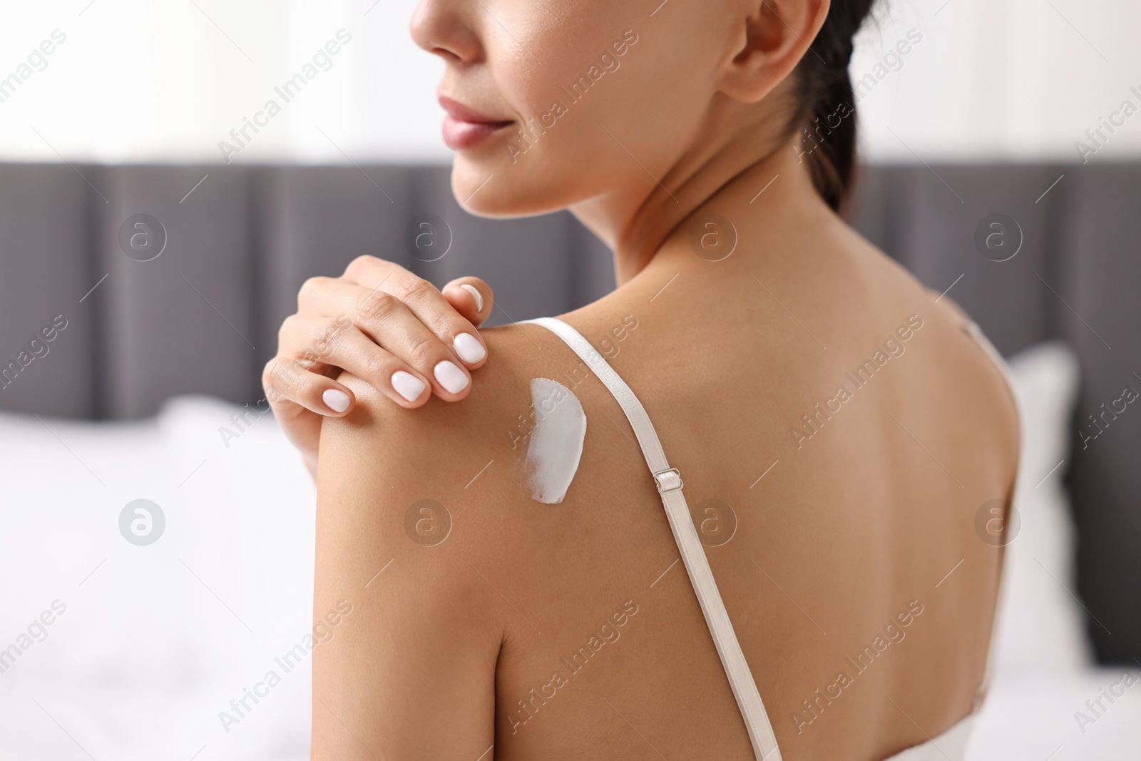 Photo of Woman applying cream onto shoulder indoors, back view. Body care