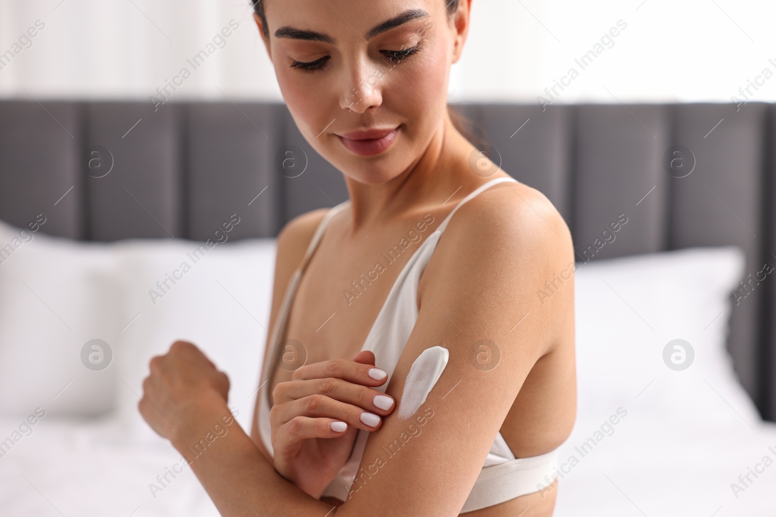 Photo of Beautiful woman applying cream onto arm indoors. Body care