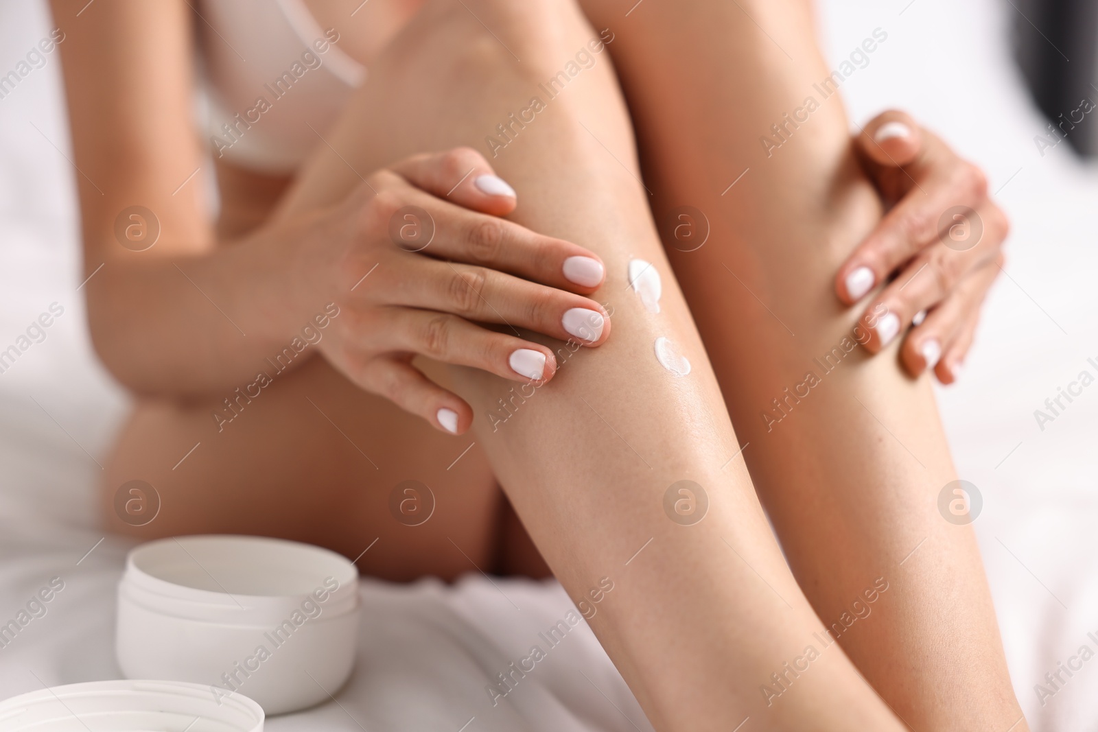 Photo of Woman applying cream onto leg on bed, closeup. Body care