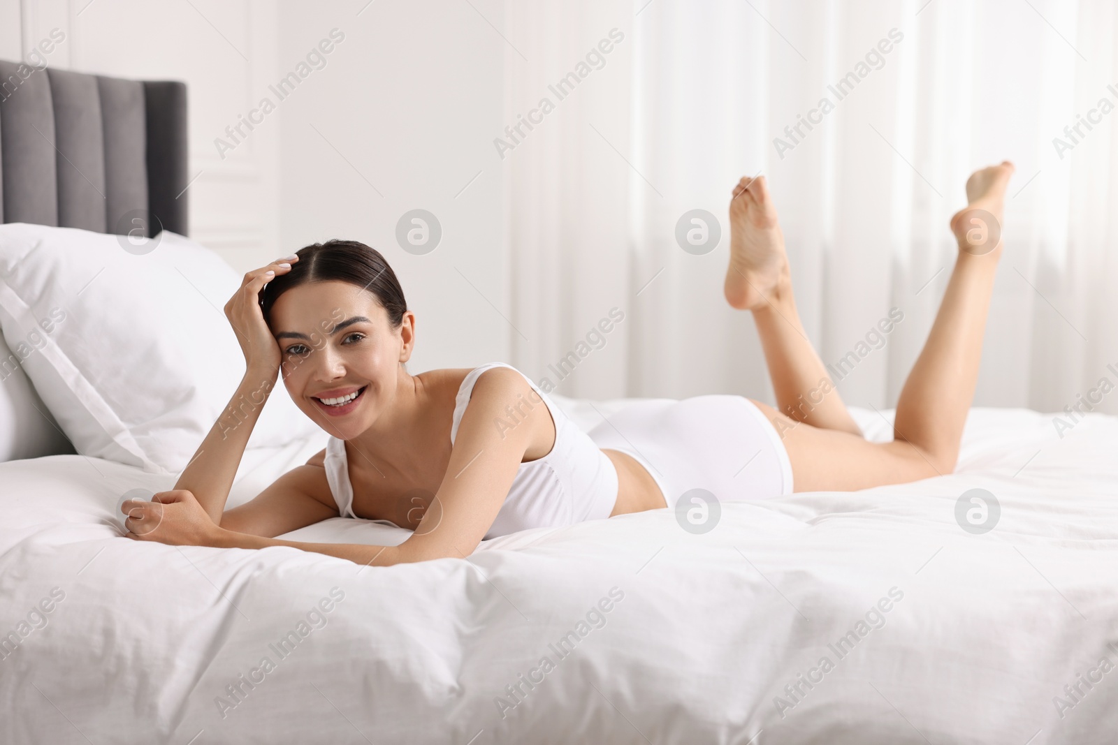 Photo of Smiling woman with perfect skin in underwear on bed. Body care