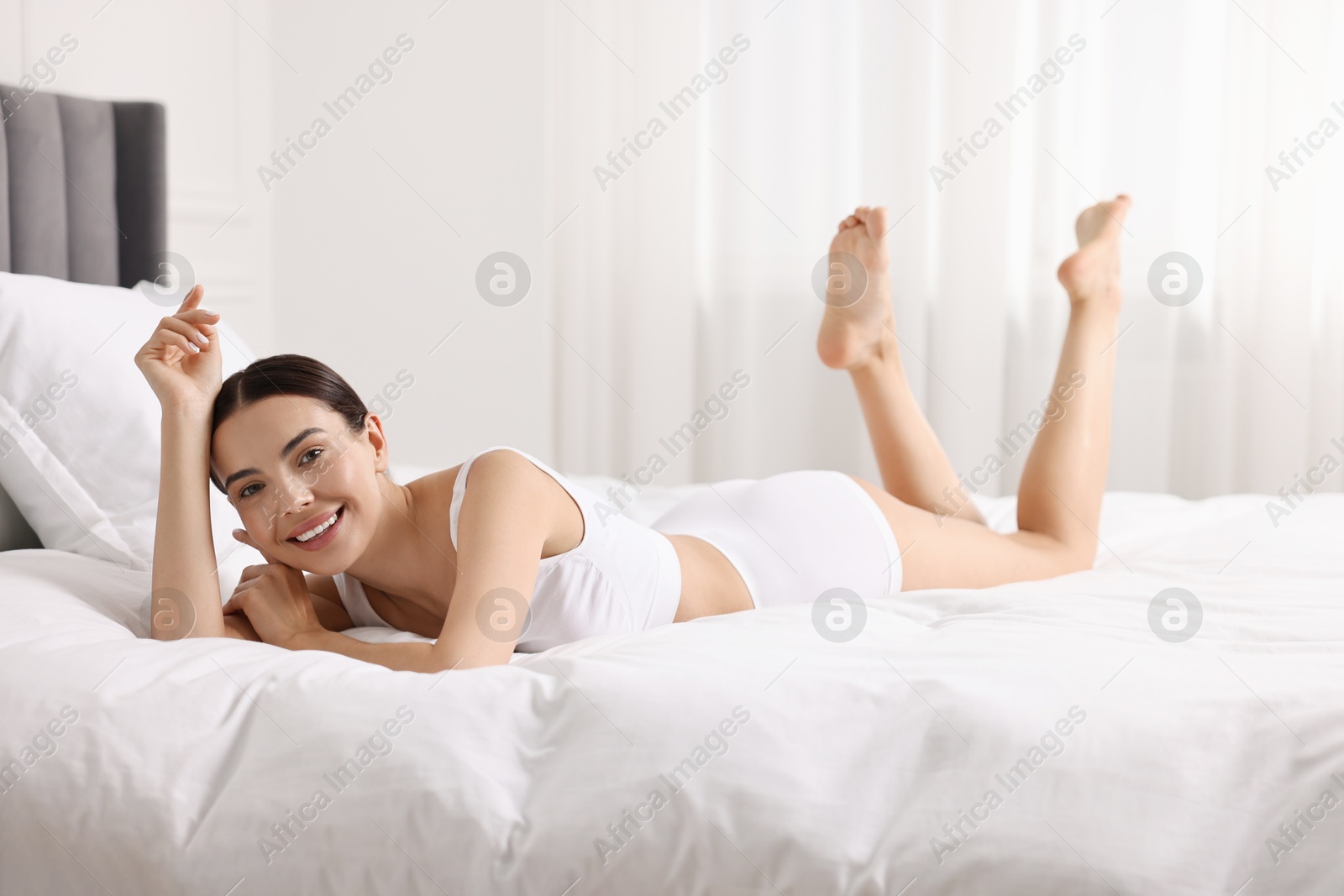 Photo of Smiling woman with perfect skin in underwear on bed. Body care