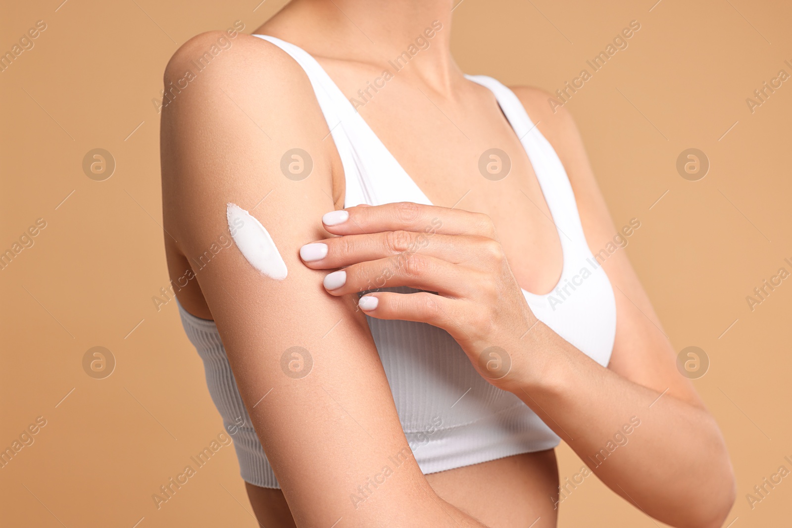 Photo of Woman applying cream onto arm on beige background, closeup. Body care