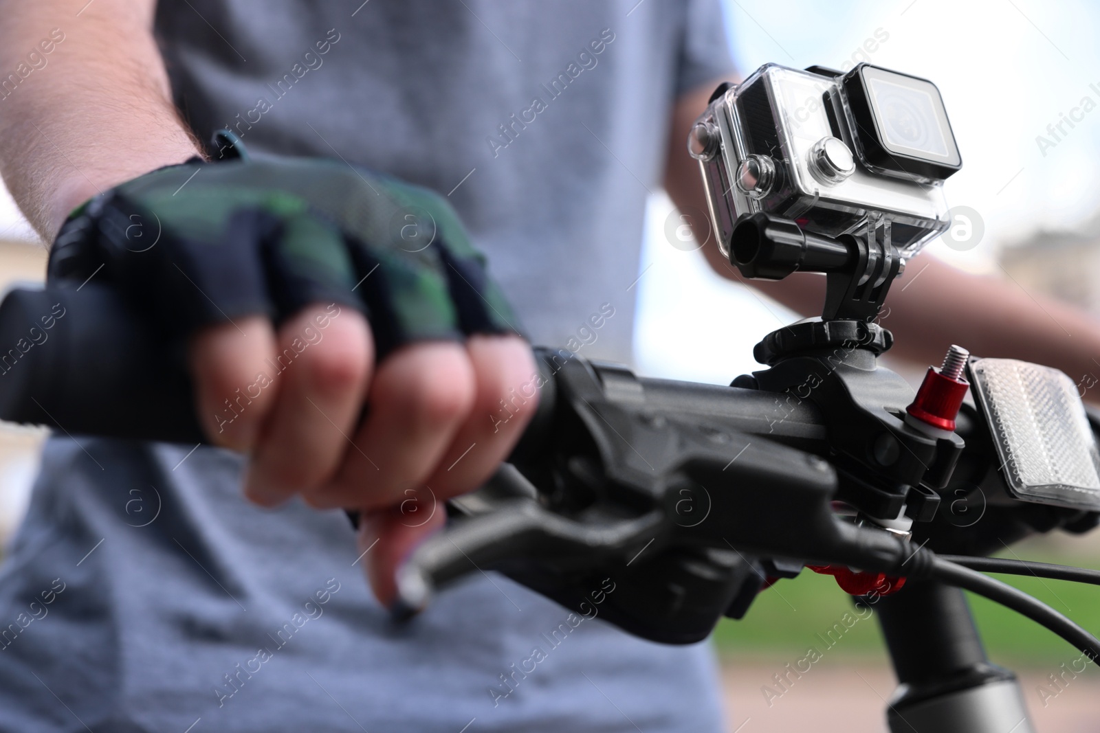 Photo of Man riding bicycle with modern action camera outdoors, closeup