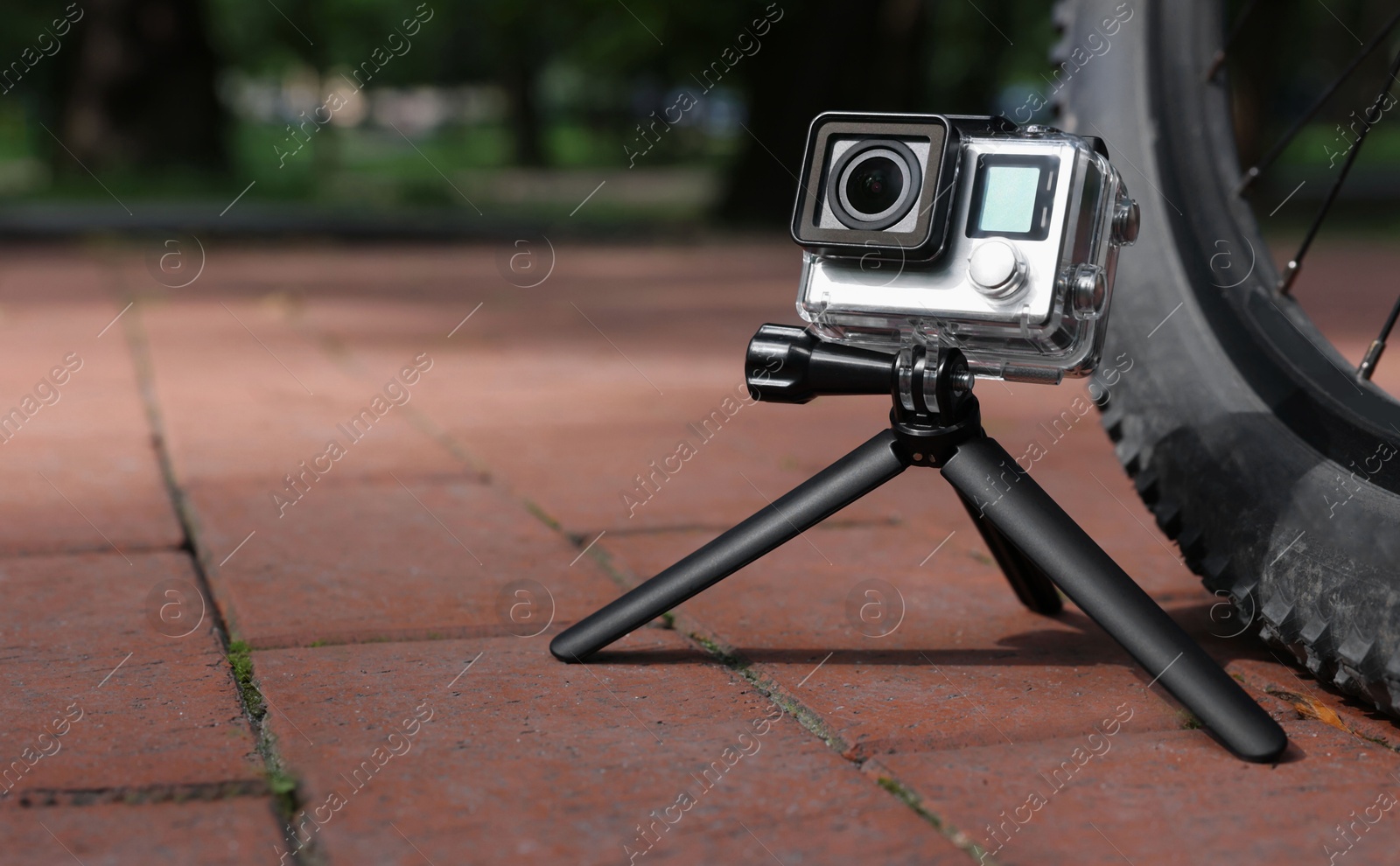 Photo of Modern action camera with tripod near bicycle outdoors. Space for text