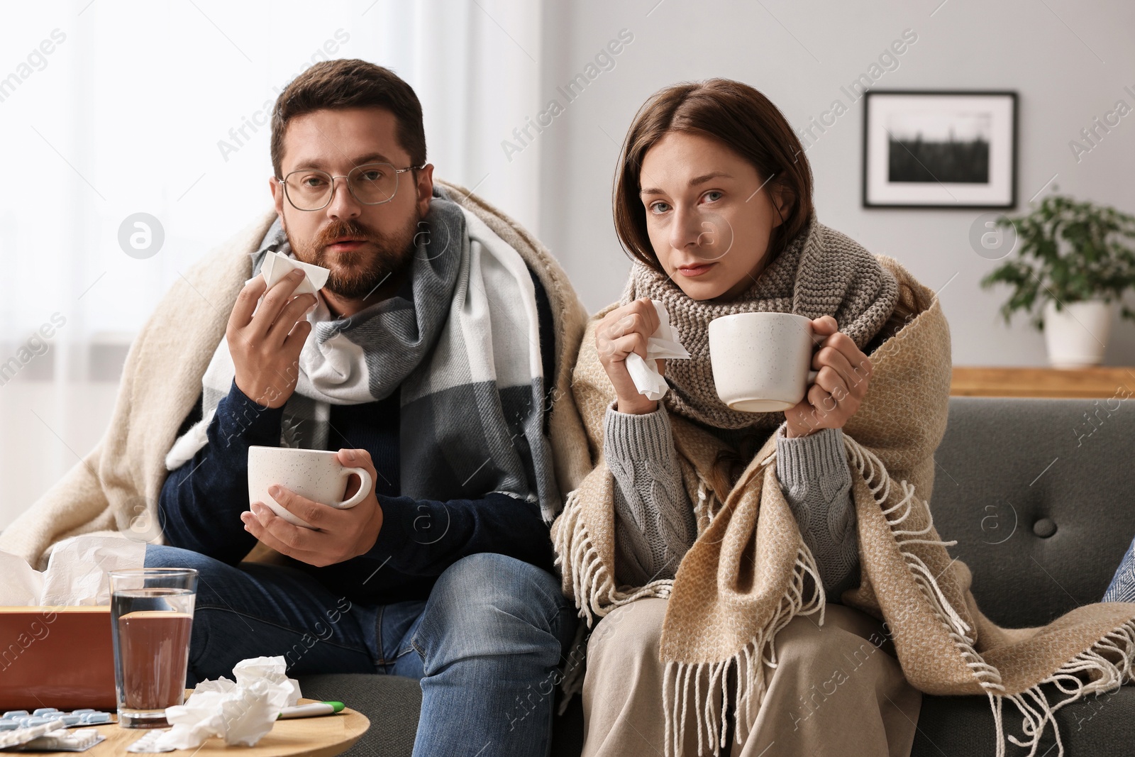 Photo of Cold symptom. Couple with cups of drink suffering from fever on sofa at home