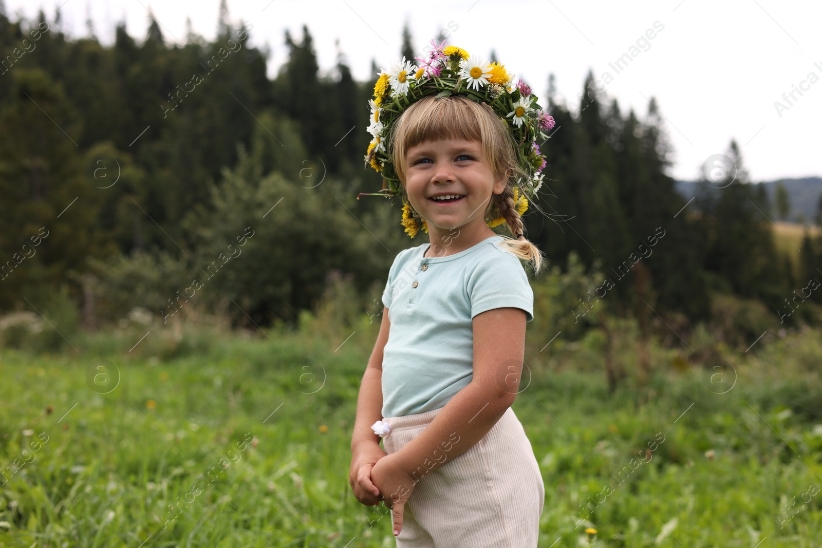 Photo of Portrait of smiling little girl in floral wreath at green meadow. Enjoying beautiful nature