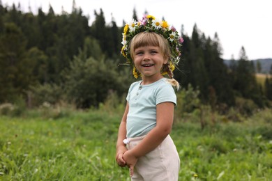 Portrait of smiling little girl in floral wreath at green meadow. Enjoying beautiful nature