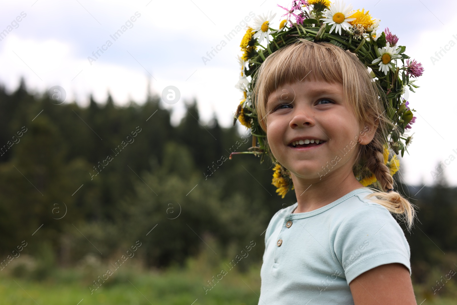 Photo of Portrait of smiling little girl in floral wreath outdoors, space for text. Enjoying beautiful nature