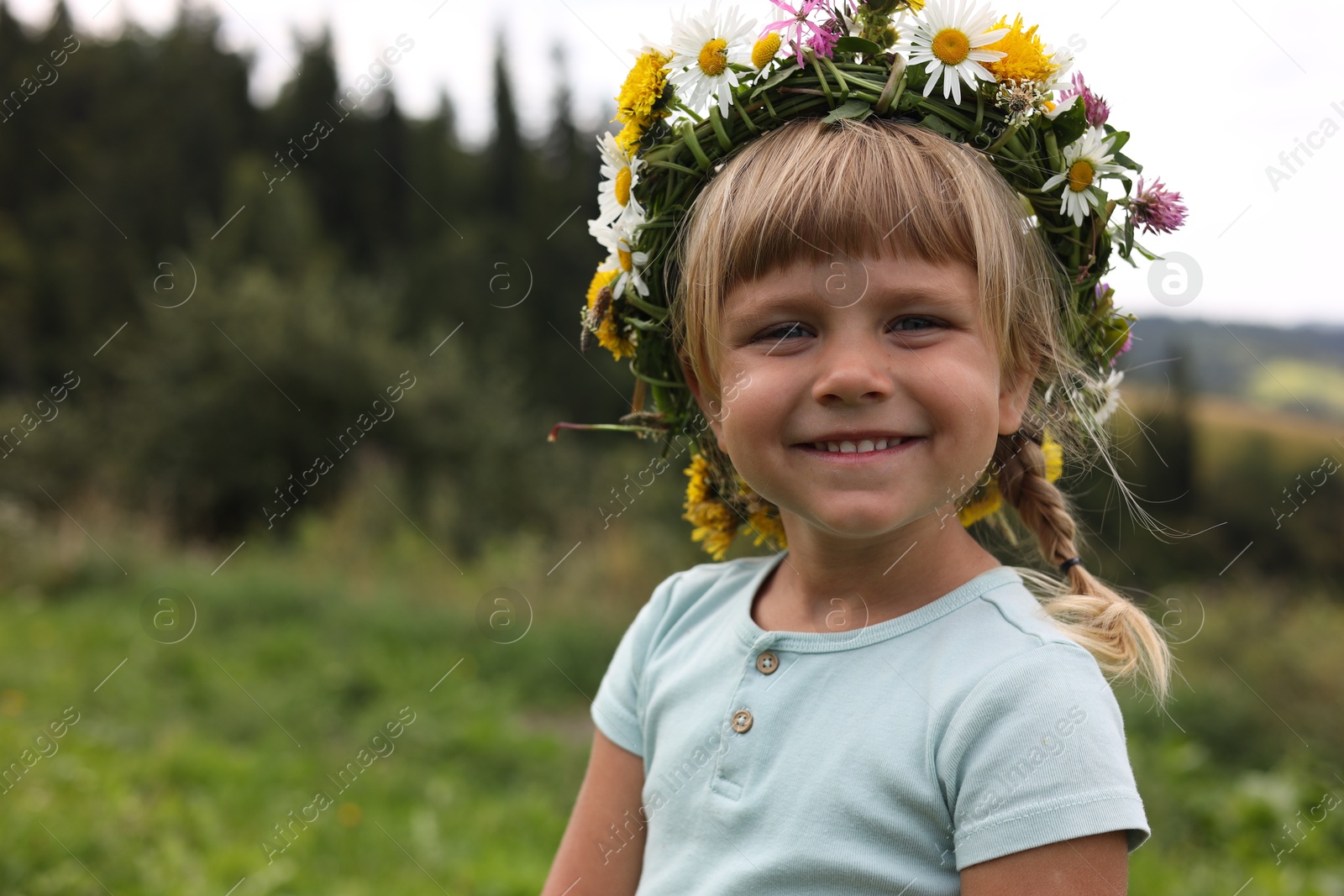 Photo of Portrait of smiling little girl in floral wreath outdoors, space for text. Enjoying beautiful nature