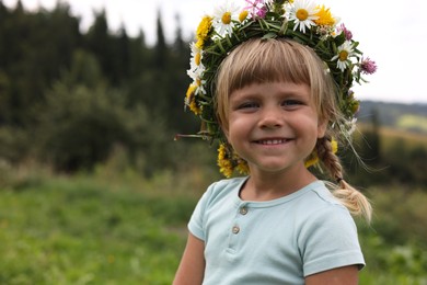 Portrait of smiling little girl in floral wreath outdoors, space for text. Enjoying beautiful nature