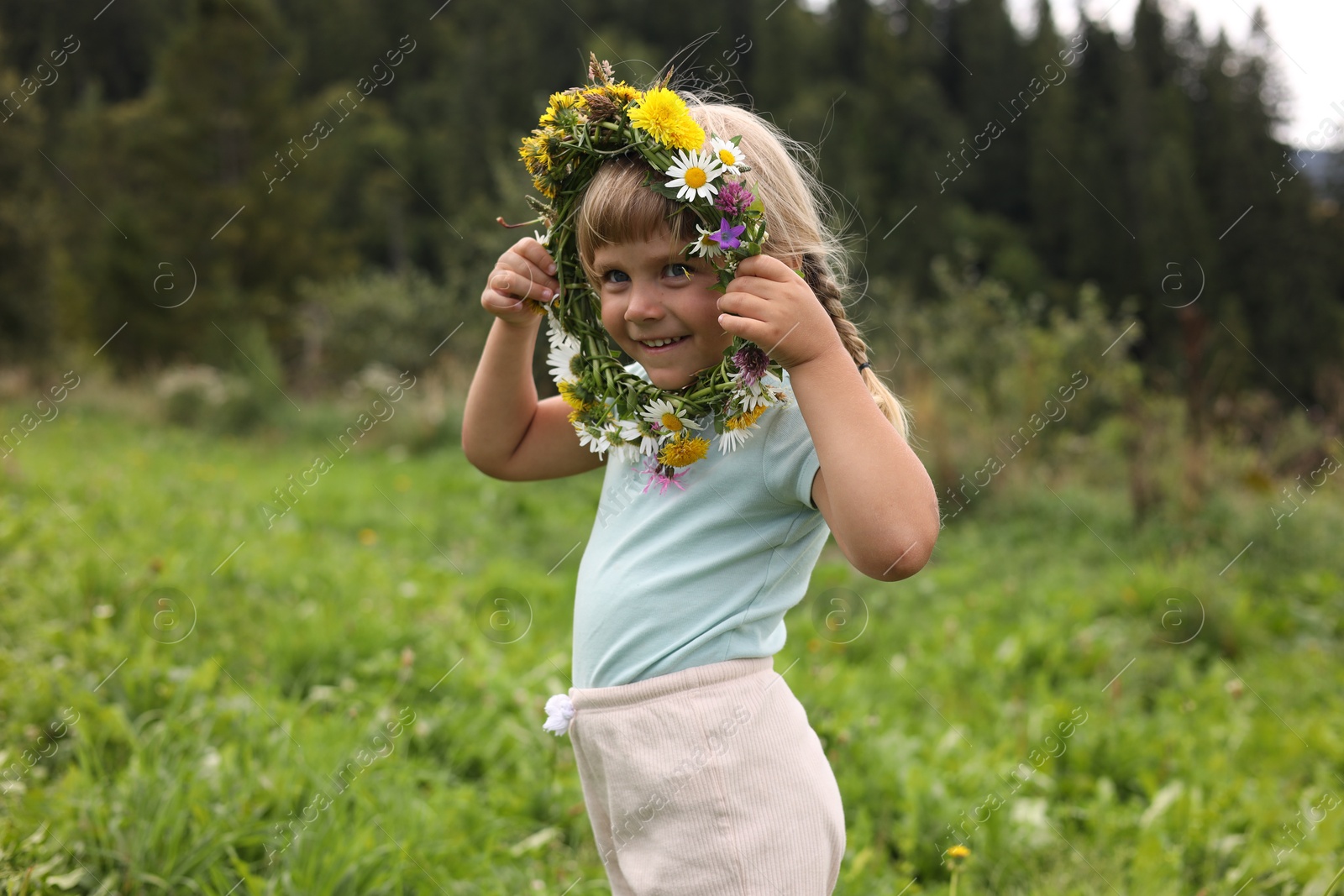 Photo of Portrait of smiling little girl with floral wreath at meadow. Enjoying beautiful nature