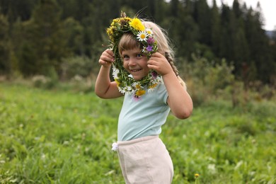 Portrait of smiling little girl with floral wreath at meadow. Enjoying beautiful nature