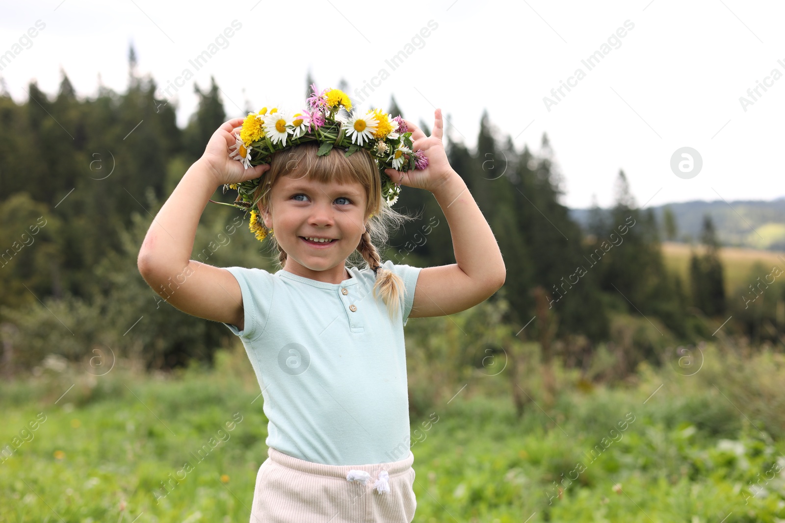 Photo of Portrait of smiling little girl in floral wreath at meadow. Enjoying beautiful nature