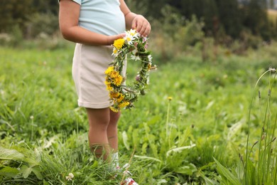 Little girl with floral wreath at meadow, closeup. Enjoying beautiful nature