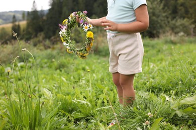 Photo of Little girl with floral wreath at meadow, closeup. Enjoying beautiful nature