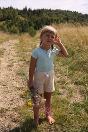 Little girl with bouquet of wildflowers outdoors on sunny day. Enjoying beautiful nature