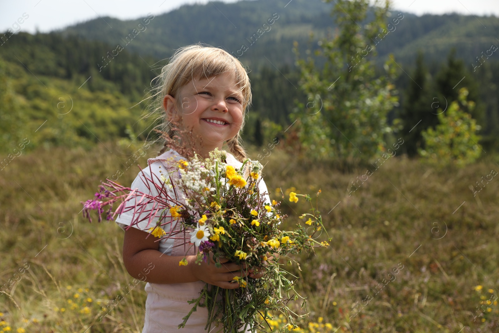 Photo of Smiling little girl with bouquet of wildflowers at field. Enjoying beautiful nature