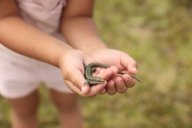 Photo of Little girl holding lizard on blurred background, closeup, space for text. Enjoying beautiful nature